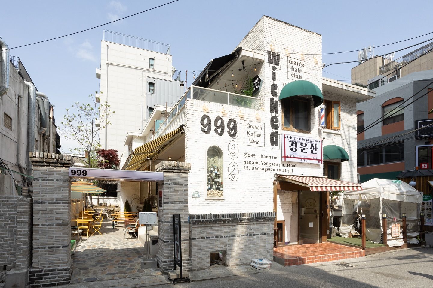 낮, 999·위키드·경운산 간판이 붙은 흰 벽돌 3층 건물과 테라스